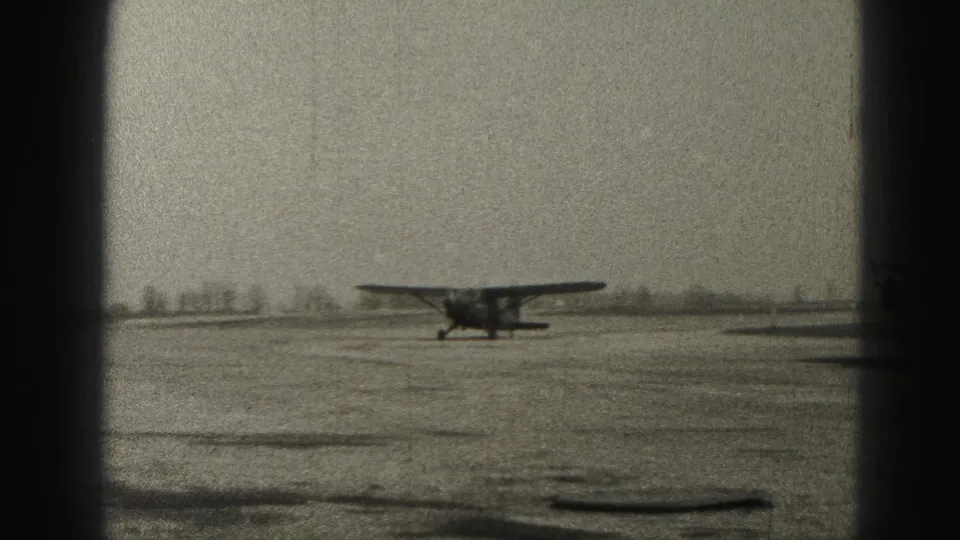 The small propeller plane appears farther along the Harrisburg runway, isolated against a low horizon in black-and-white 8mm footage from 1946.