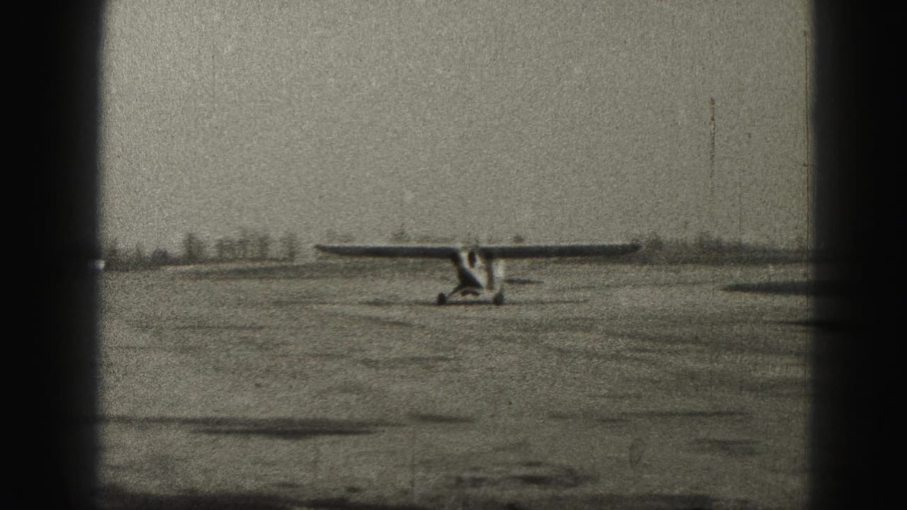 Small propeller plane farther along the runway, framed by dark vertical film borders.