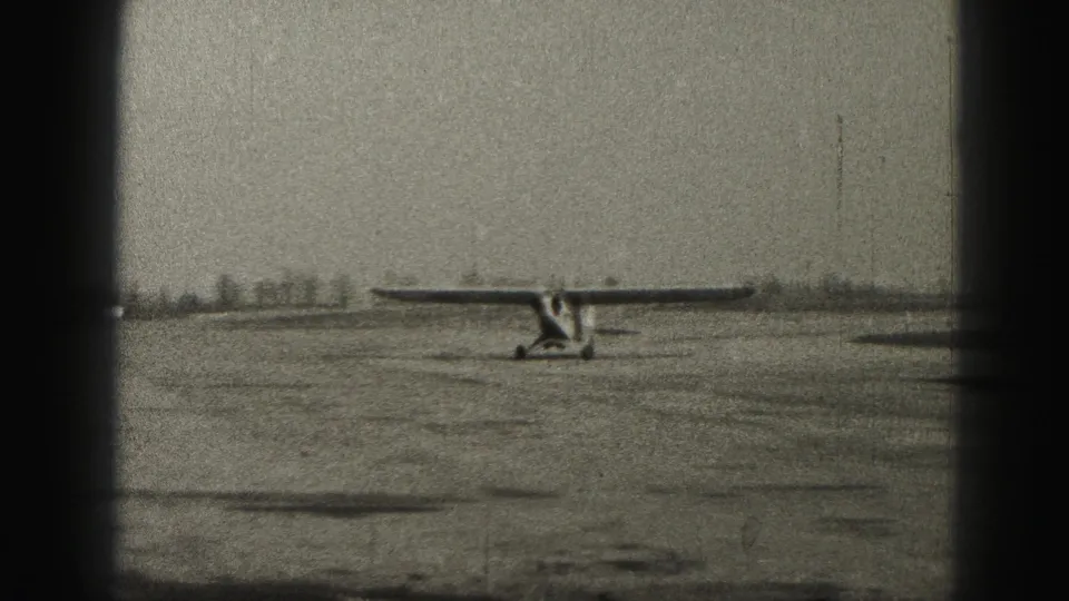 The charter plane continues taxiing across the rural Harrisburg airfield, with distant low shapes near the horizon and visible 8mm wear.