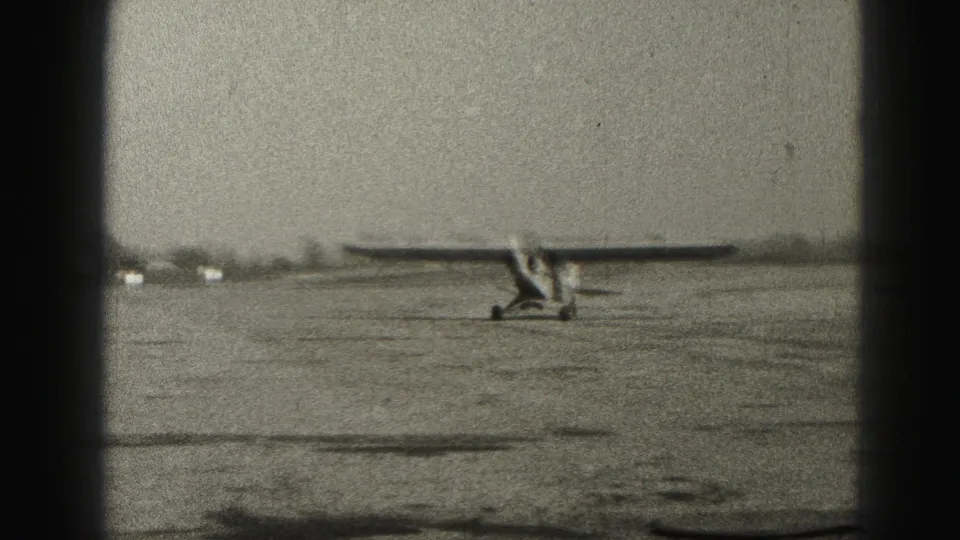 A small single-engine plane passes through the frame on the Harrisburg airfield, captured with grain, soft focus, and heavy 8mm gate borders.