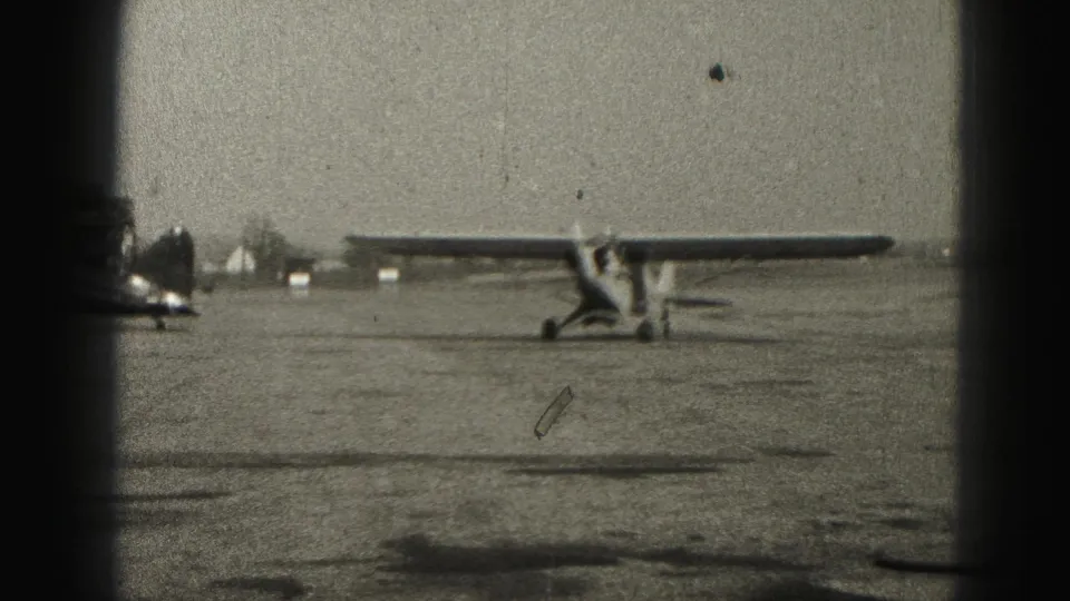 1946 Harrisburg airfield view with a light airplane near a darker aircraft on a sunlit paved apron.