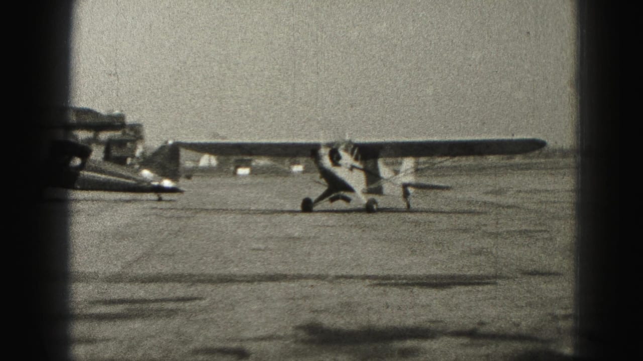 A light airplane stands beside a darker parked aircraft on an open airfield.