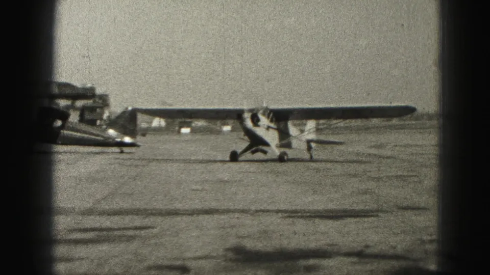 Small light aircraft and darker airplane parked side by side on a Harrisburg, Pennsylvania airfield in 1946 footage.