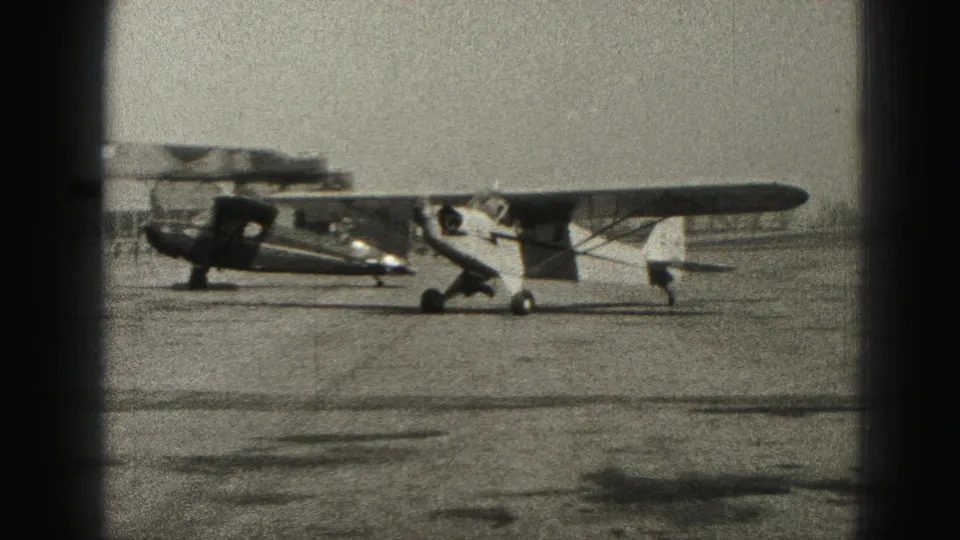 Side view of a small light airplane near a darker aircraft on a 1946 Harrisburg airport apron.