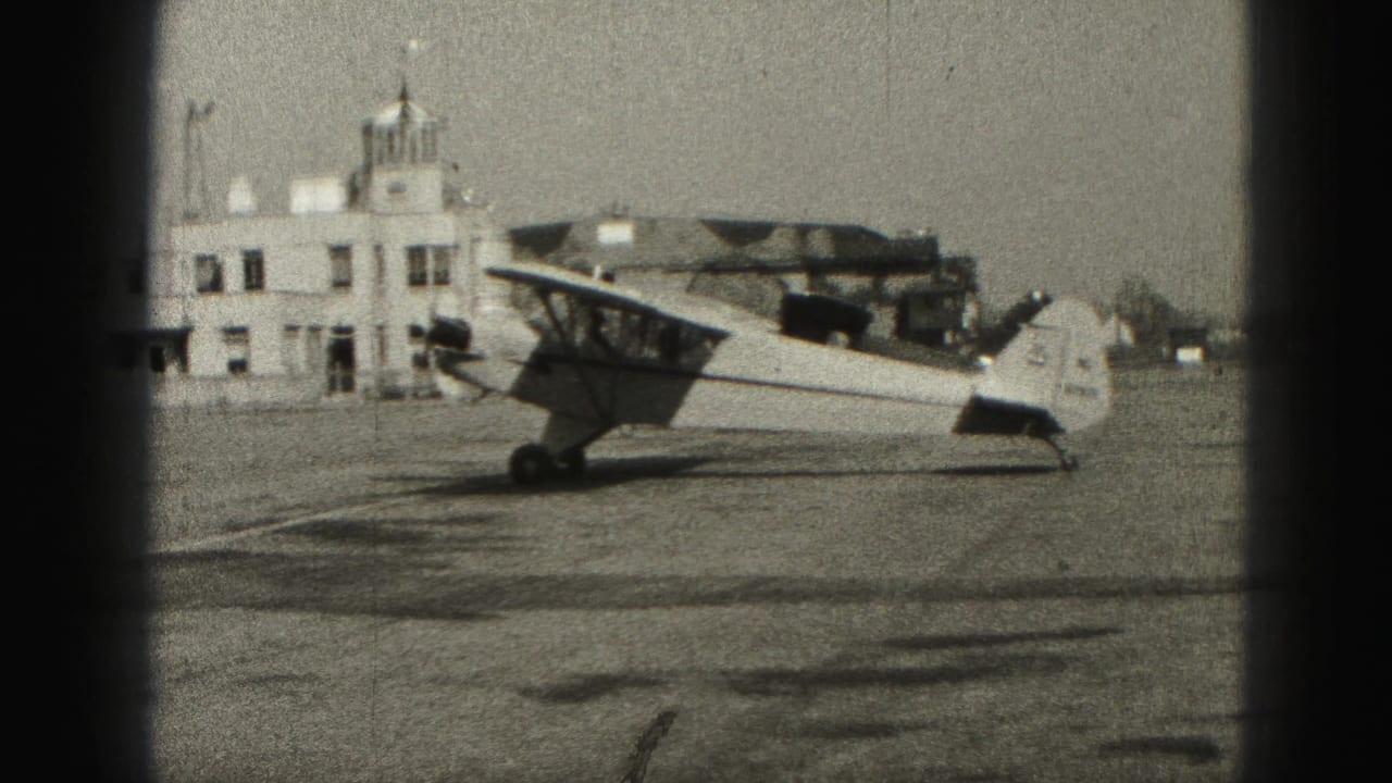 Side view of a small single-engine aircraft at a Harrisburg airfield in 1946, with a low white building in the background.