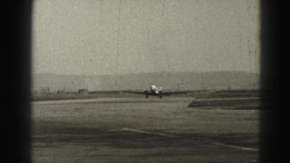 Small aircraft taxiing in the distance on a Harrisburg-area runway, captured in grainy black-and-white 8mm footage.