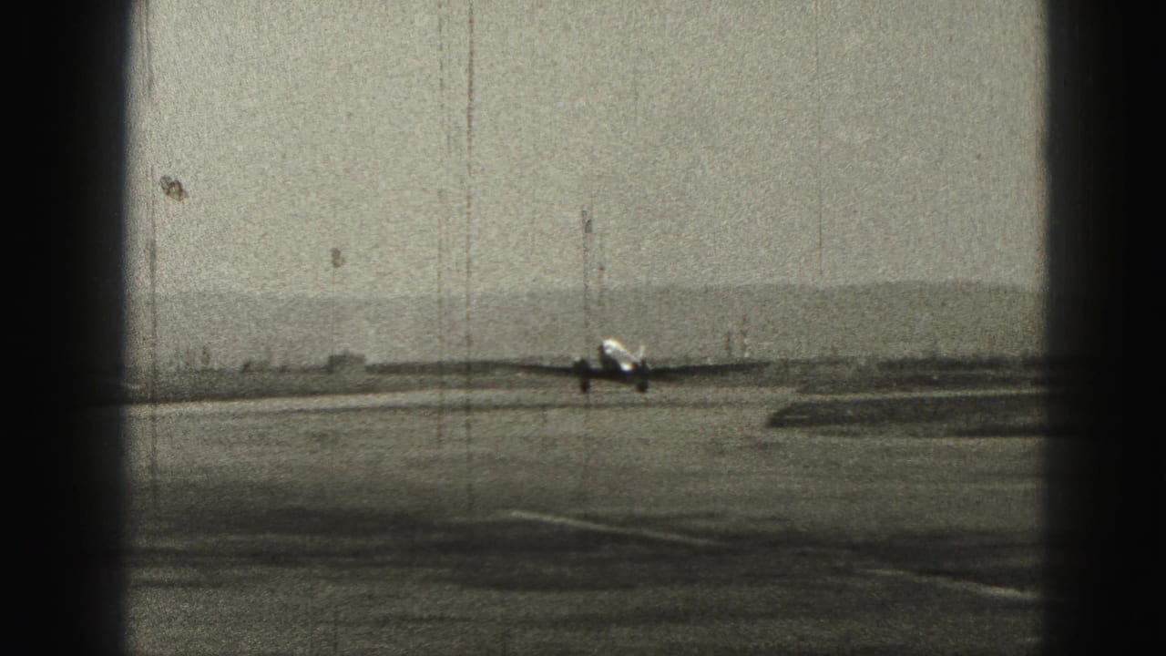 Twin-engine propeller airplane approaching a runway in a grainy 8mm frame.