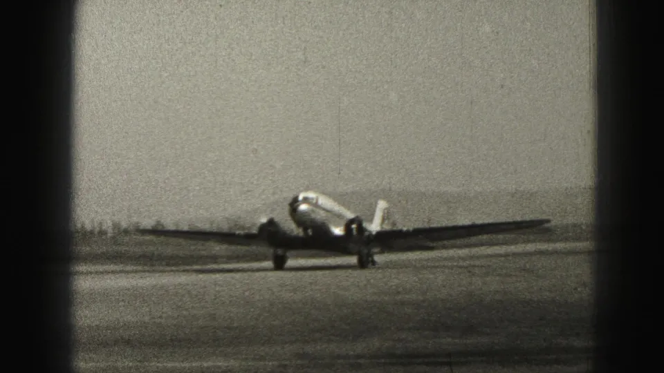 A twin-engine propeller aircraft taxis along the Harrisburg runway, framed by dark 8mm film borders and visible grain.
