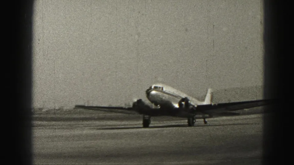 1946 Harrisburg home-movie frame showing a twin-engine propeller airplane taxiing on an open runway under a gray sky.