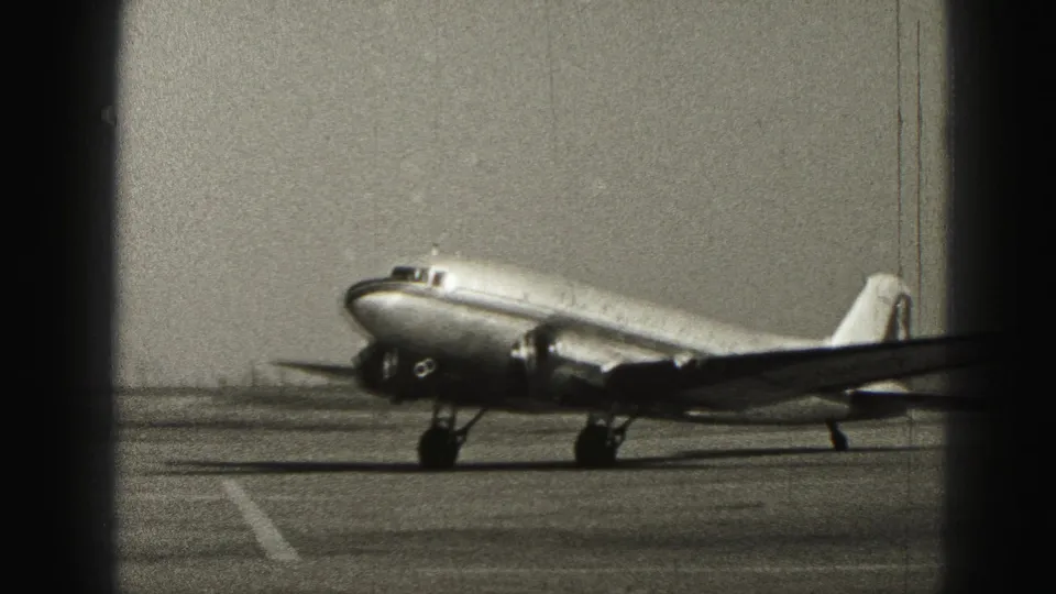 1946 Harrisburg 8mm frame with a closer side-front view of a twin-engine propeller aircraft moving along the runway.
