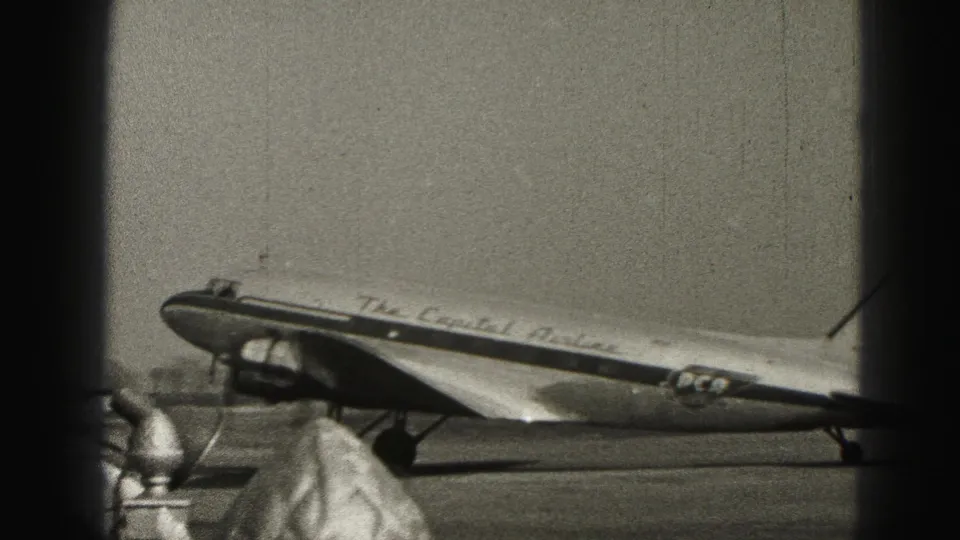 The Capital Airlines DC-3 remains parked at Harrisburg as people stand near the aircraft in grainy black-and-white footage.