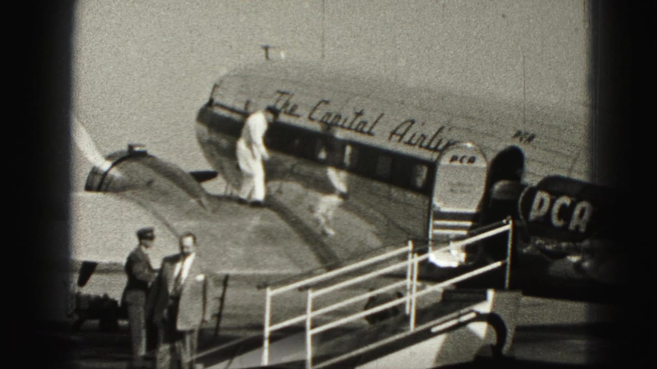 Passengers board a DC-3 aircraft by mobile stairs as crew stand near the fuselage.