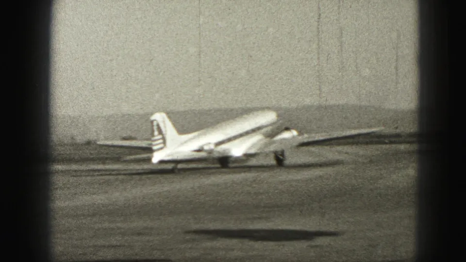 1946 Harrisburg 8mm frame showing a passenger plane moving on the runway with distant hills and dark film-edge vignetting.