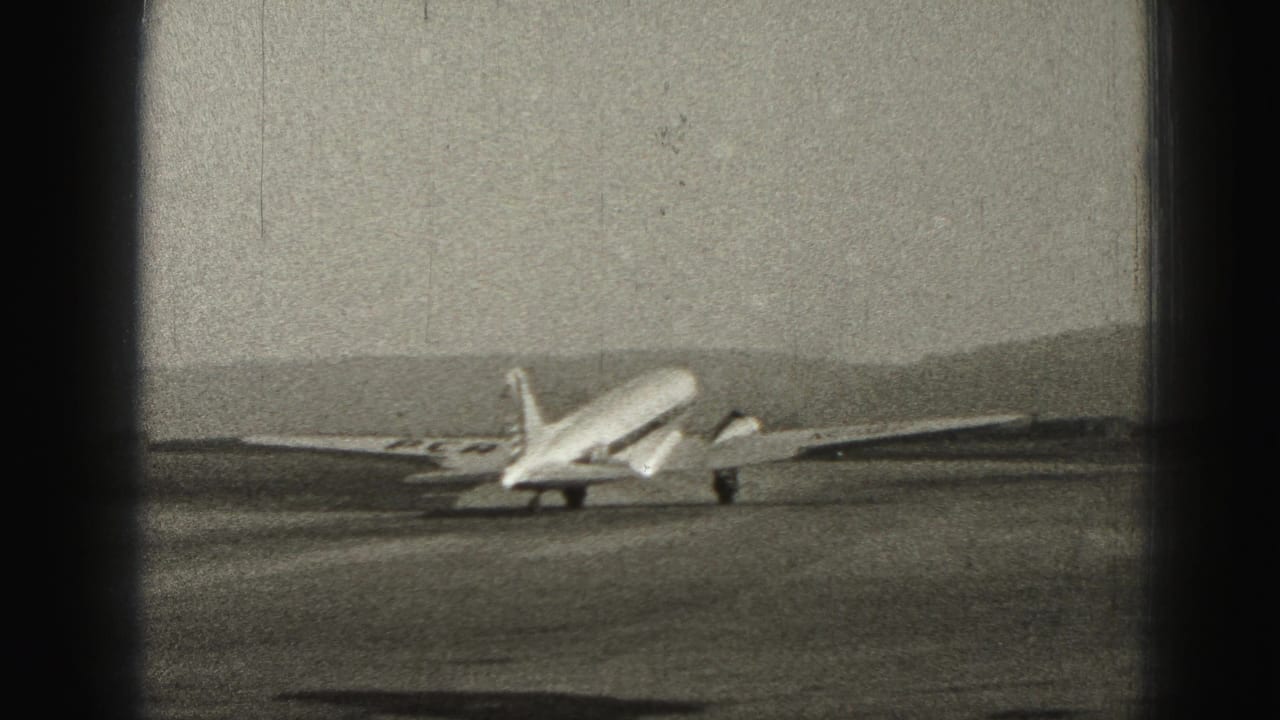 Passenger plane taxis across an open runway below distant hills.