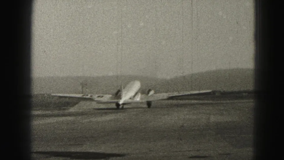 Rear 8mm view of the 1946 Harrisburg passenger plane moving away along the runway, with hills and heavy film texture visible.