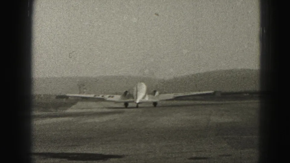 1946 Harrisburg home-movie frame showing the passenger aircraft from behind near takeoff, with runway, hills, and visible 8mm edge darkening.