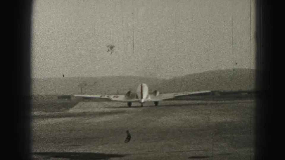 A small propeller airplane appears on a Harrisburg, Pennsylvania runway in 1946, seen through dark 8mm frame borders with distant hills beyond.