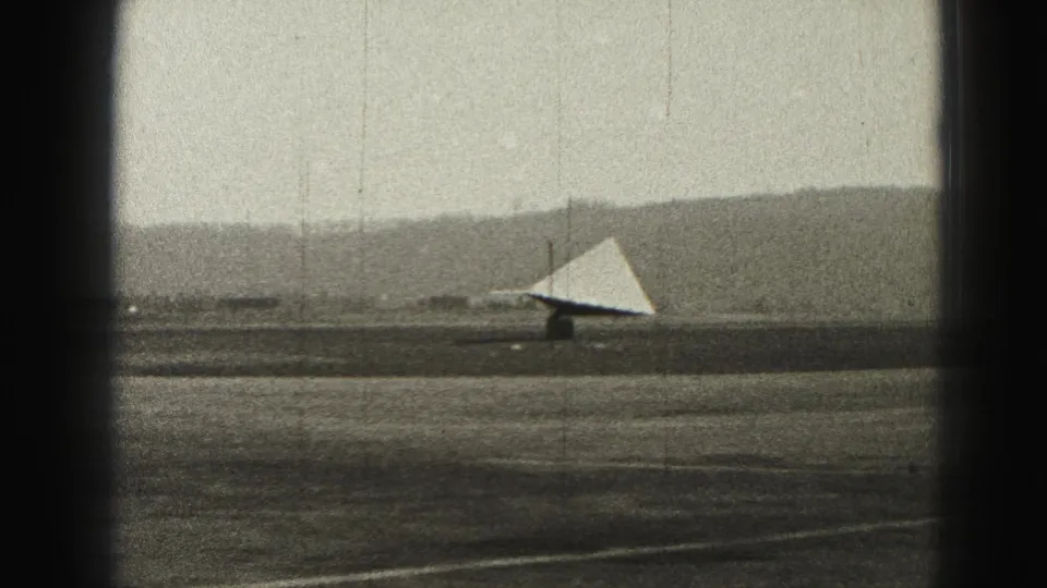 A distant 1946 Harrisburg runway scene shows a triangular light-toned aircraft surface or structure against low hills and a flat airfield.