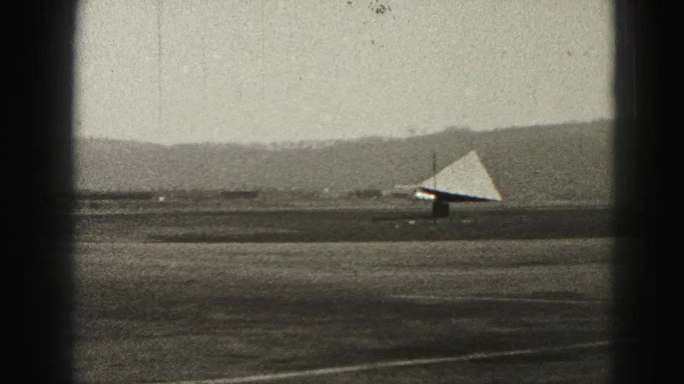At the end of the 1946 Harrisburg runway clip, a small light triangular aircraft shape remains distant against the airfield and hills.