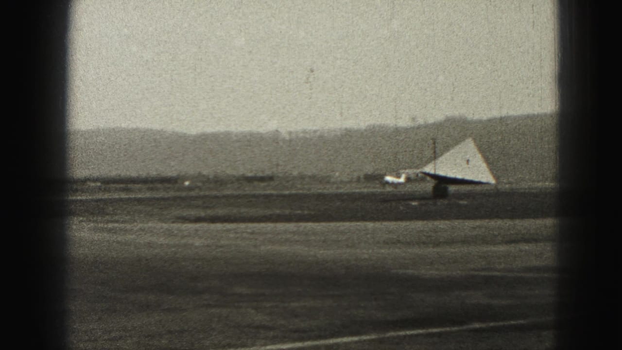 Small airplane on a runway beside a triangular glider-like object, with hills in the distance.