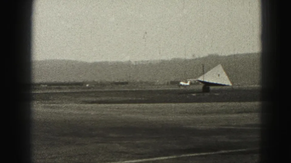 1946 Harrisburg airport scene showing a small airplane on the runway near a triangular glider-like object, framed by dark 8mm borders.