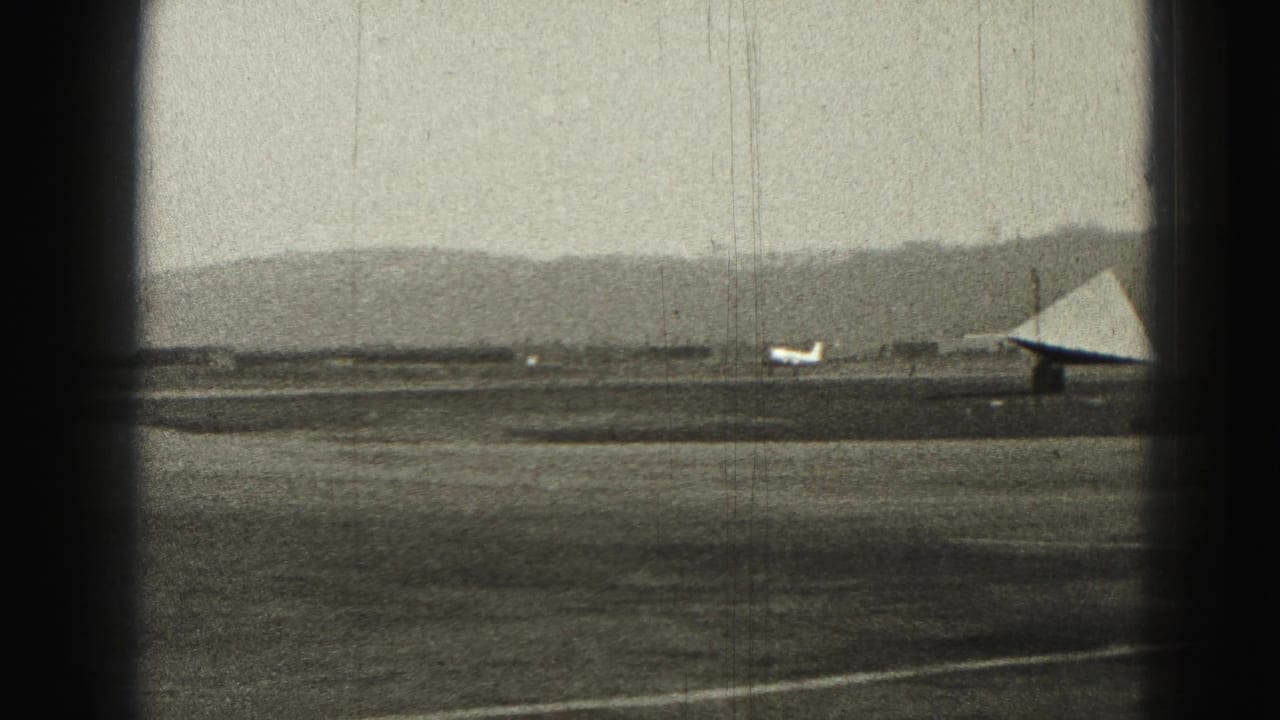 Small airplane farther along the runway, with a triangular structure at right and distant hills.