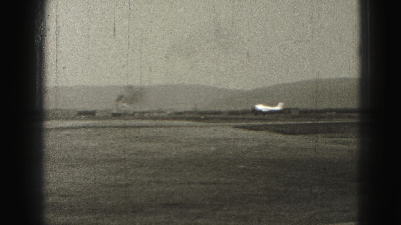 Small airplane on a distant runway seen through dark vertical frame edges.