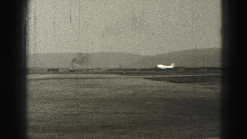 1946 8mm home-movie frame from Harrisburg showing a small propeller airplane low on a distant runway under a hazy sky.