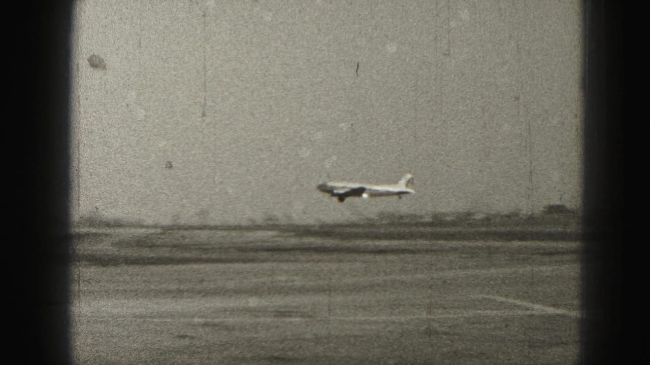 Small airplane landing on a runway seen through dark film borders.