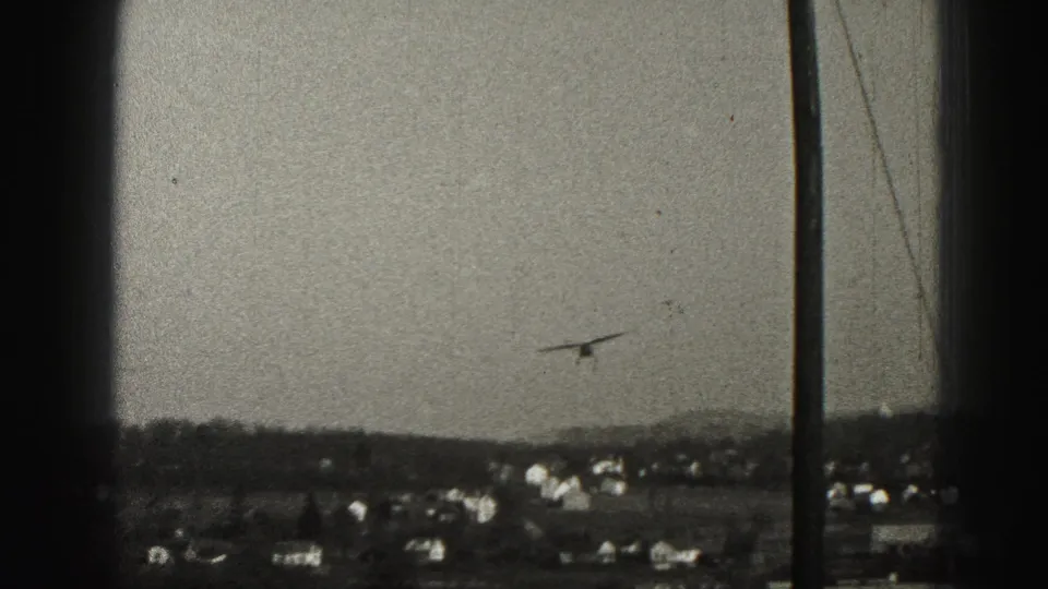 A small aircraft descends over Harrisburg-area houses, with a utility pole in the foreground of the 1946 8mm frame.