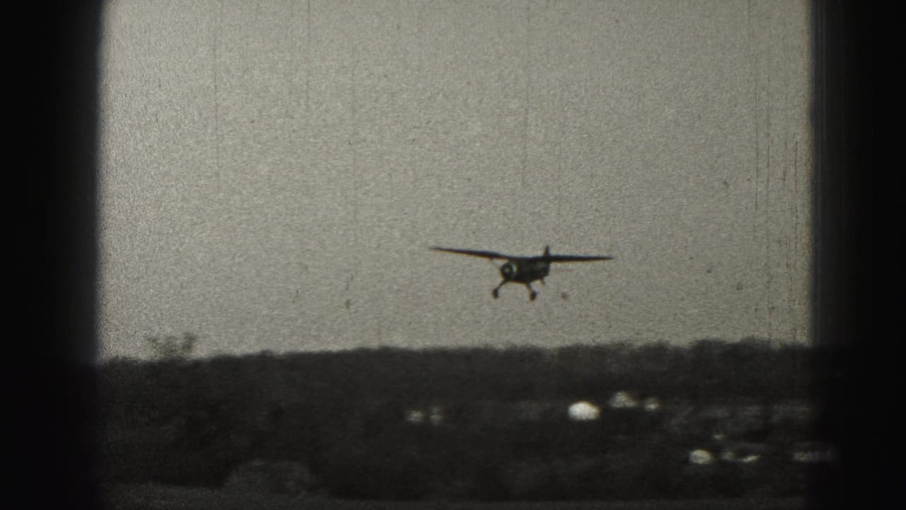 Small propeller plane approaching above a low rural horizon with dark frame edges.