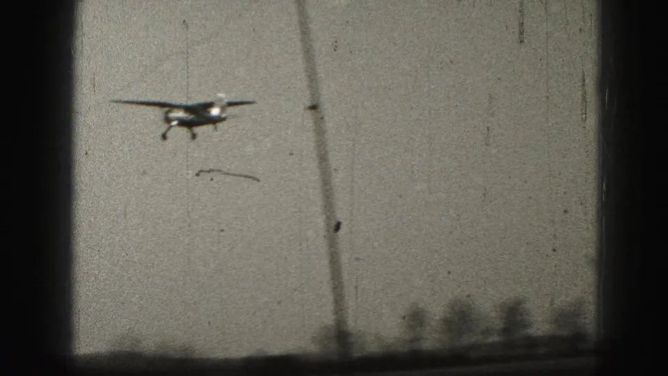 A distant small plane descends against the sky near Harrisburg, with a low horizon and visible film wear.