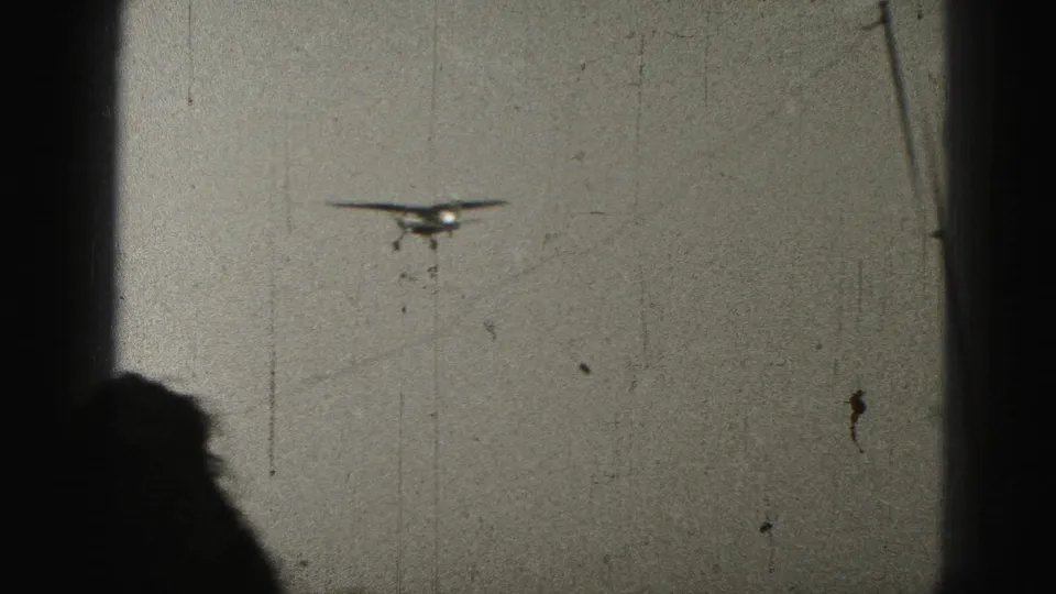 Small airplane in flight over Harrisburg, Pennsylvania, seen through dark framing in grainy 1946 8mm footage.