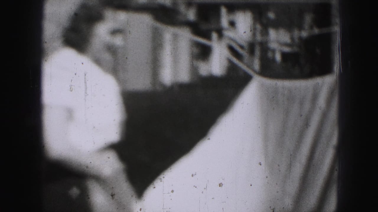 Woman in a light dress stands beside a hanging sheet near a backyard clothesline.
