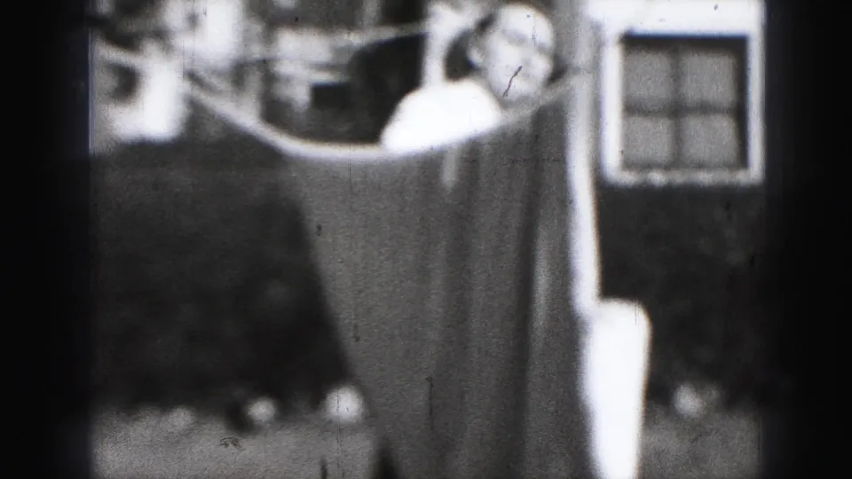 A woman in a light dress is partly framed by a hanging sheet and a house window in the 1946 Harrisburg backyard scene.