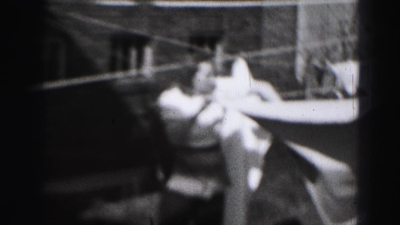 Woman reaches toward a clothesline with laundry stretched across the yard.