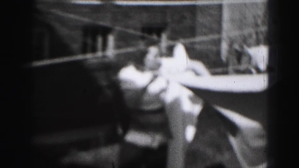 A woman in a light dress reaches up to hang or adjust laundry on a backyard clothesline in Harrisburg, Pennsylvania.