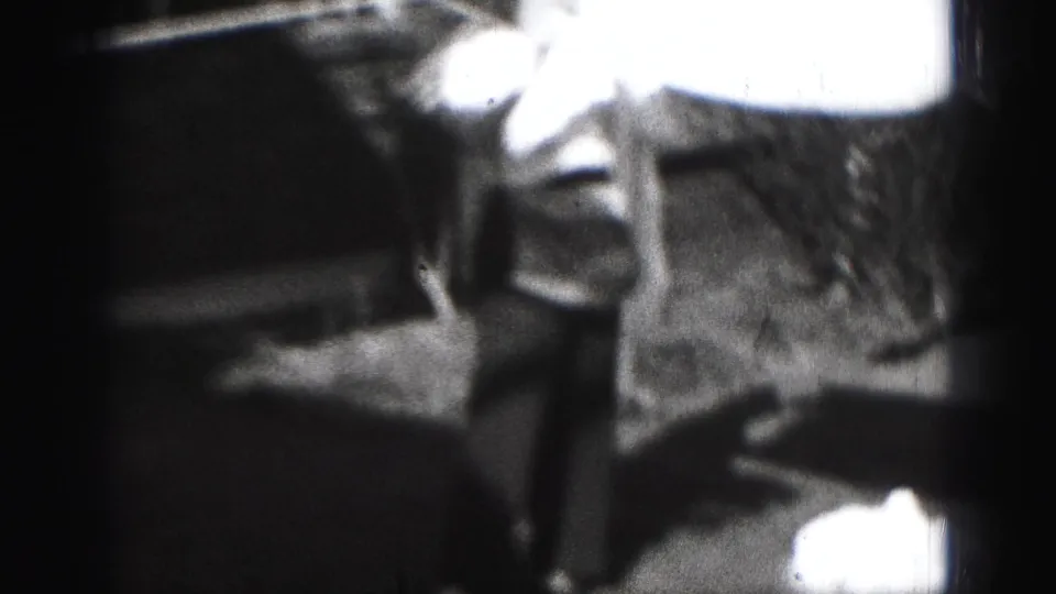 The woman continues handling laundry outdoors, with overexposed fabric close to the camera and darker yard areas behind her.