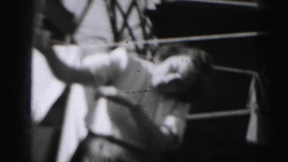 The 1946 home-movie frame shows the woman securing laundry on a backyard line, with a railing or steps behind her.