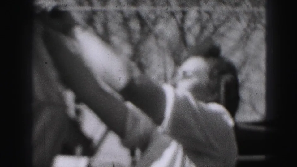 A close, soft 8mm view shows the woman lifting a white sheet while working at the backyard clothesline in Harrisburg.