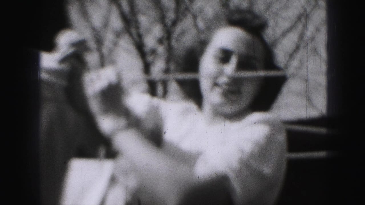 In 1946 Harrisburg home-movie footage, a woman in a light dress lifts laundry beside a backyard clothesline with bare branches behind her.