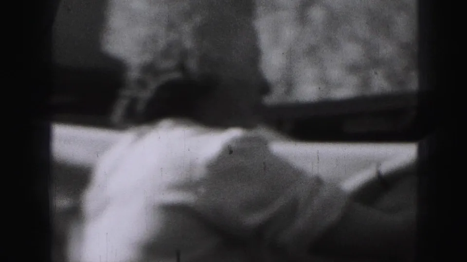 A soft, blurred 8mm frame shows light-colored laundry near the backyard clothesline, with the woman mostly obscured by motion and framing.