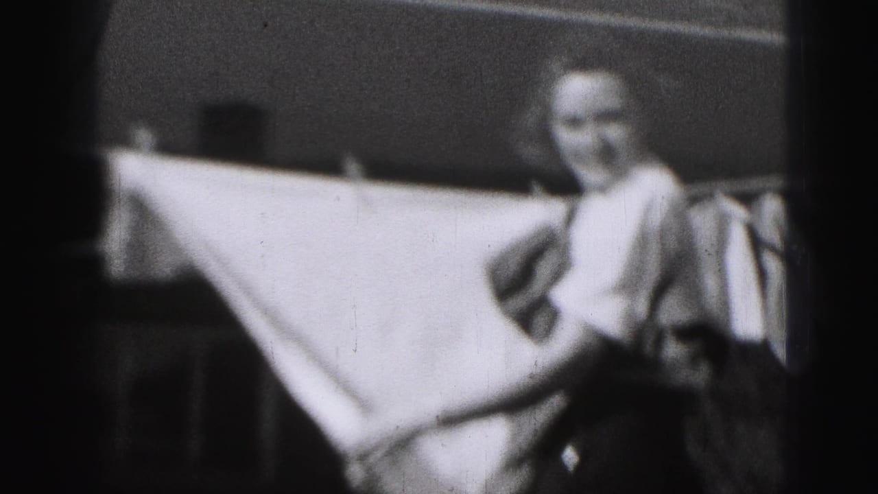 Woman standing outdoors near a clothesline while holding a large white sheet.