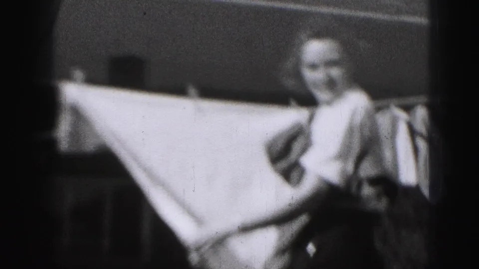 In 1946 Harrisburg home-movie footage, a woman stands by an outdoor clothesline with a large white sheet stretched across the frame.