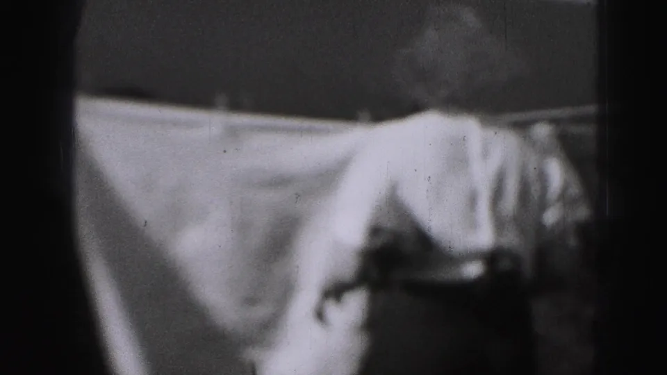 A white sheet fills much of the frame on an outdoor clothesline, with the woman partly visible at the right edge in the 1946 home movie.