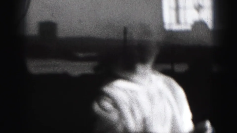 1946 Harrisburg home-movie frame showing a baby in a light shirt seen close up in a shadowed interior with a bright window behind.