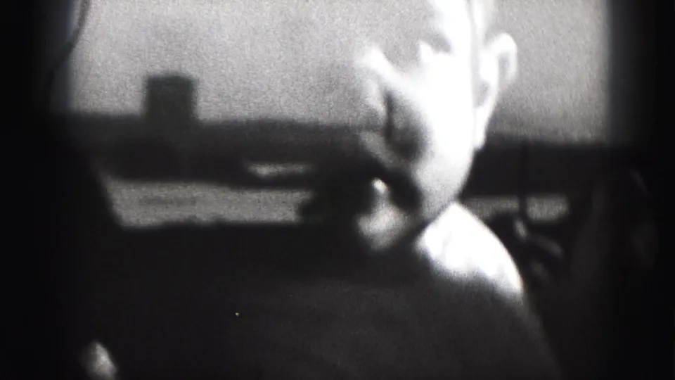 Grainy black-and-white frame from the Harrisburg clip showing the baby bending sideways in a dim room with indistinct furniture behind.
