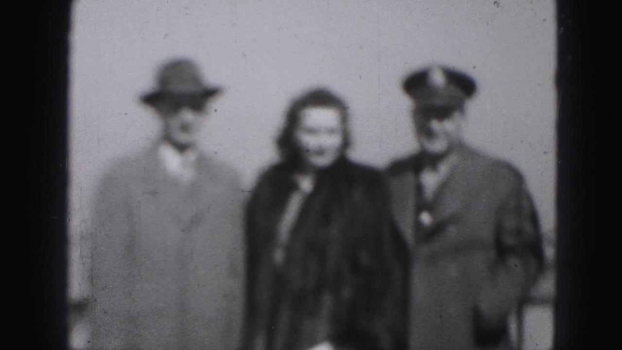 Three adults face the camera, with a woman between two men, one in a fedora and one in a peaked cap.