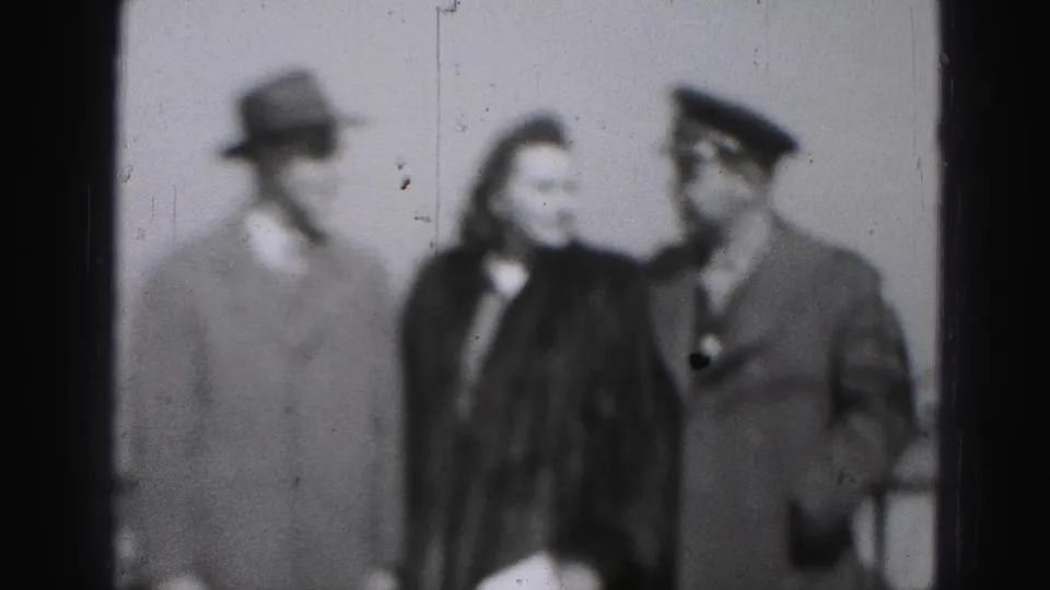 In the 1946 Harrisburg footage, the posed group shifts as the woman turns toward the uniform-capped man beside her.