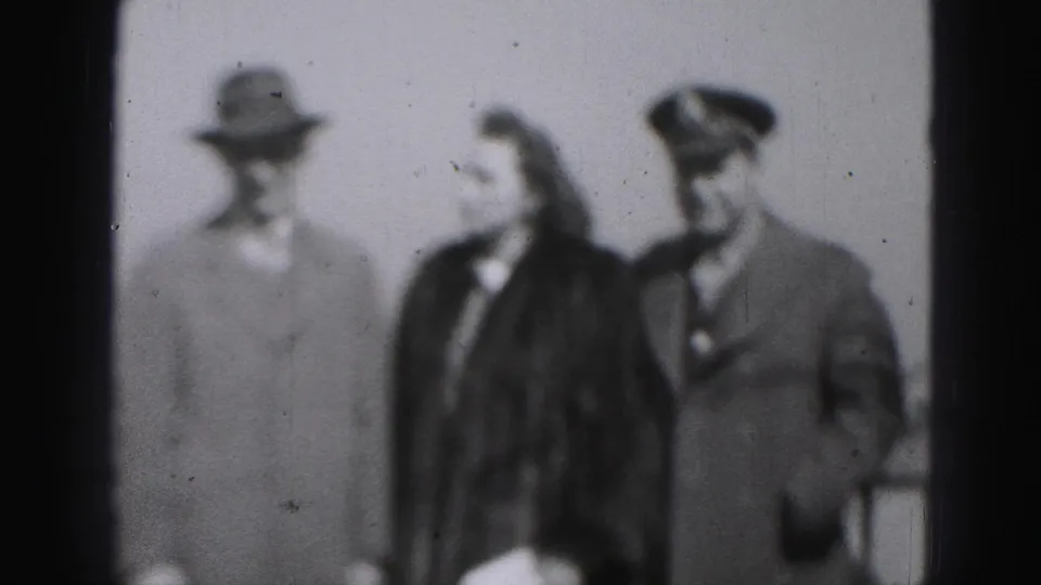Soft black-and-white 1946 Harrisburg frame showing a woman walking between a fedora-wearing man and a man in a peaked cap.